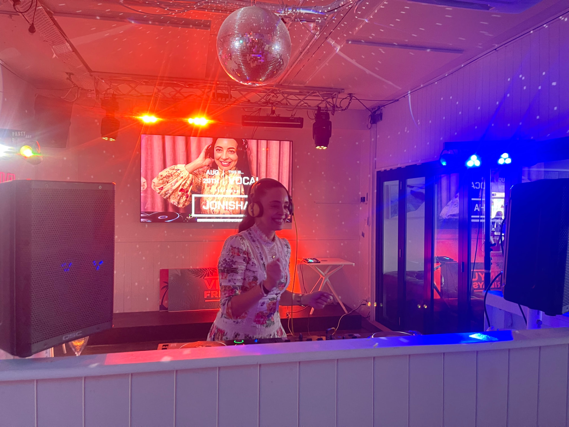 JoNisha performing behind the DJ booth at a red-and-blue-lit Perth nightclub