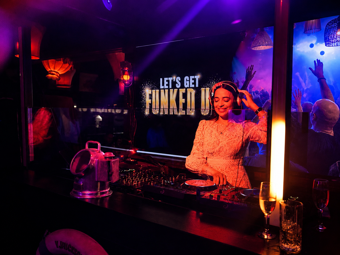 JoNisha mixing in a warmly lit lounge with the crowd on screen behind her